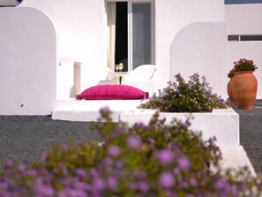 A white outdoor seating area with a pink cushion, a white chair, and a small table with a glass. There are potted plants with purple flowers in the foreground. - Sesmarias Turismo Rural & SPA (Cuba)