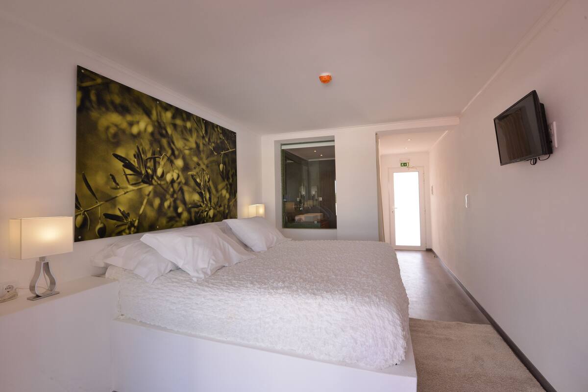 Habitación de hotel moderna con una cama grande, un televisor montado en la pared y un cuadro abstracto de gran tamaño.