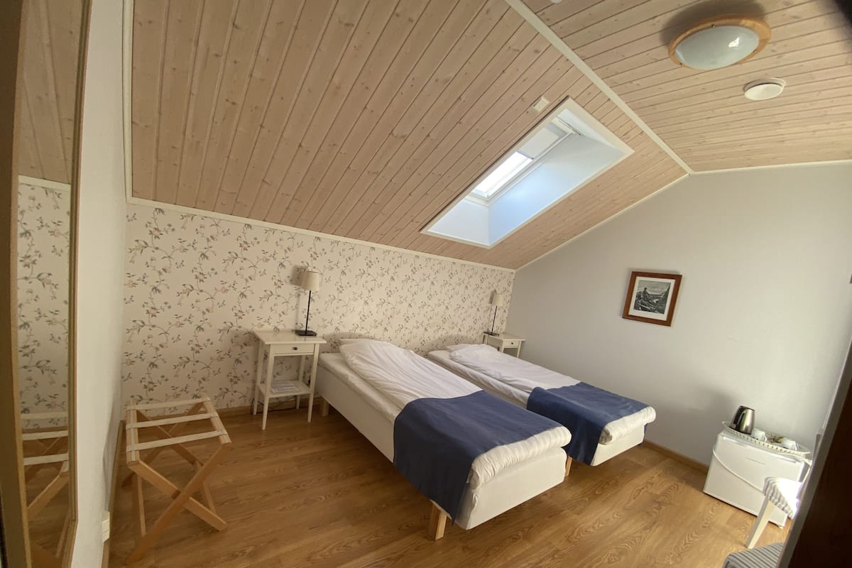 Ein Zimmer mit zwei Betten, einem Oberlicht, Holzboden, einem kleinen Schreibtisch und einer Heizung.