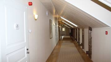 A corridor with wooden flooring, white walls, and a sloped ceiling.