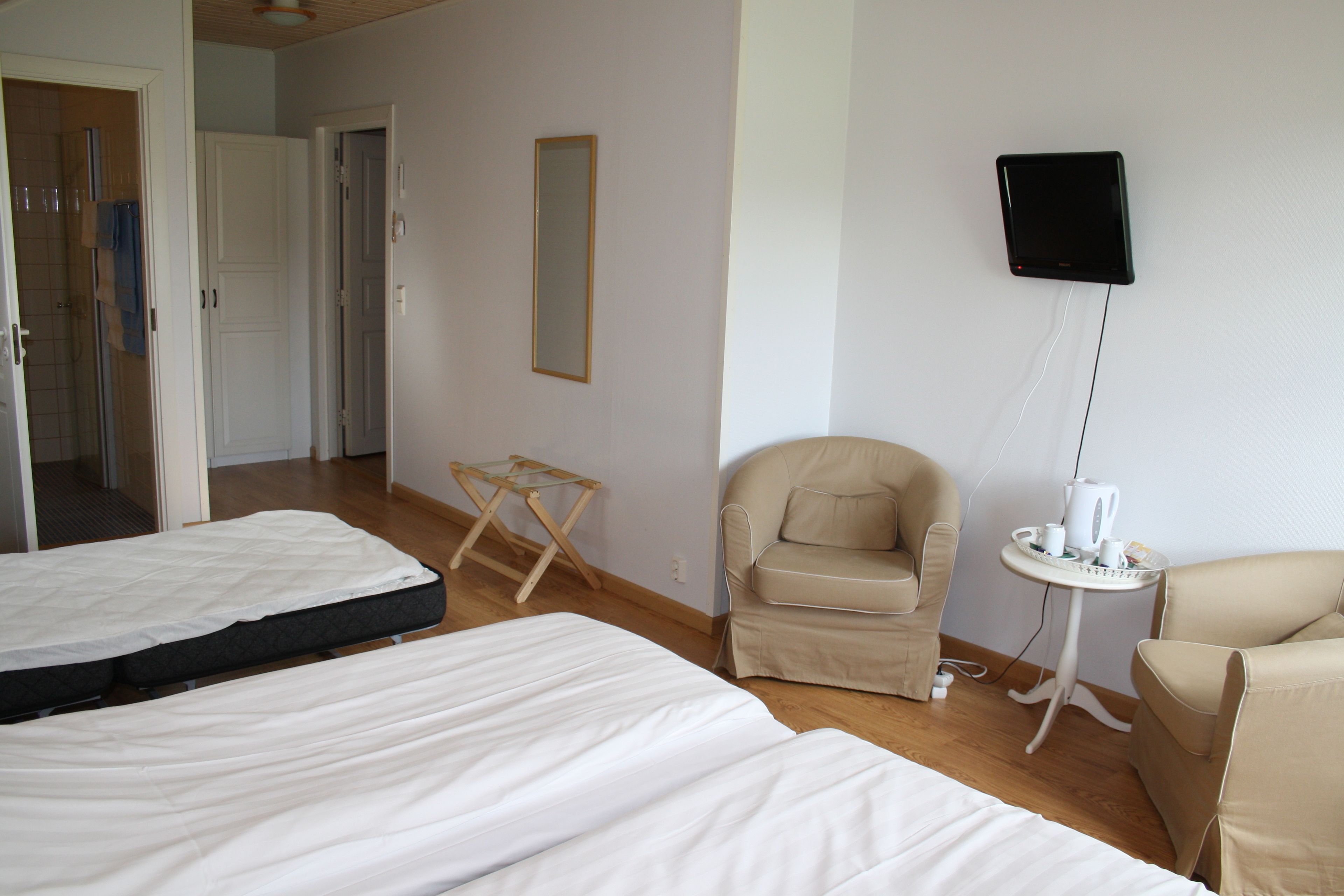 Habitación de hotel con dos camas, una silla, una mesita con una tetera y un televisor montado en la pared.