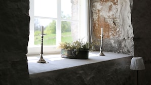 Una habitación rústica con una ventana, una planta en maceta y dos candelabros sobre un repisa.