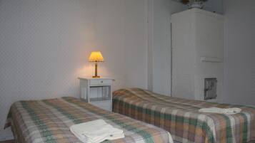 A room with two beds, each with a plaid bedspread and a folded towel on the bed. There is a nightstand with a lamp between the beds.