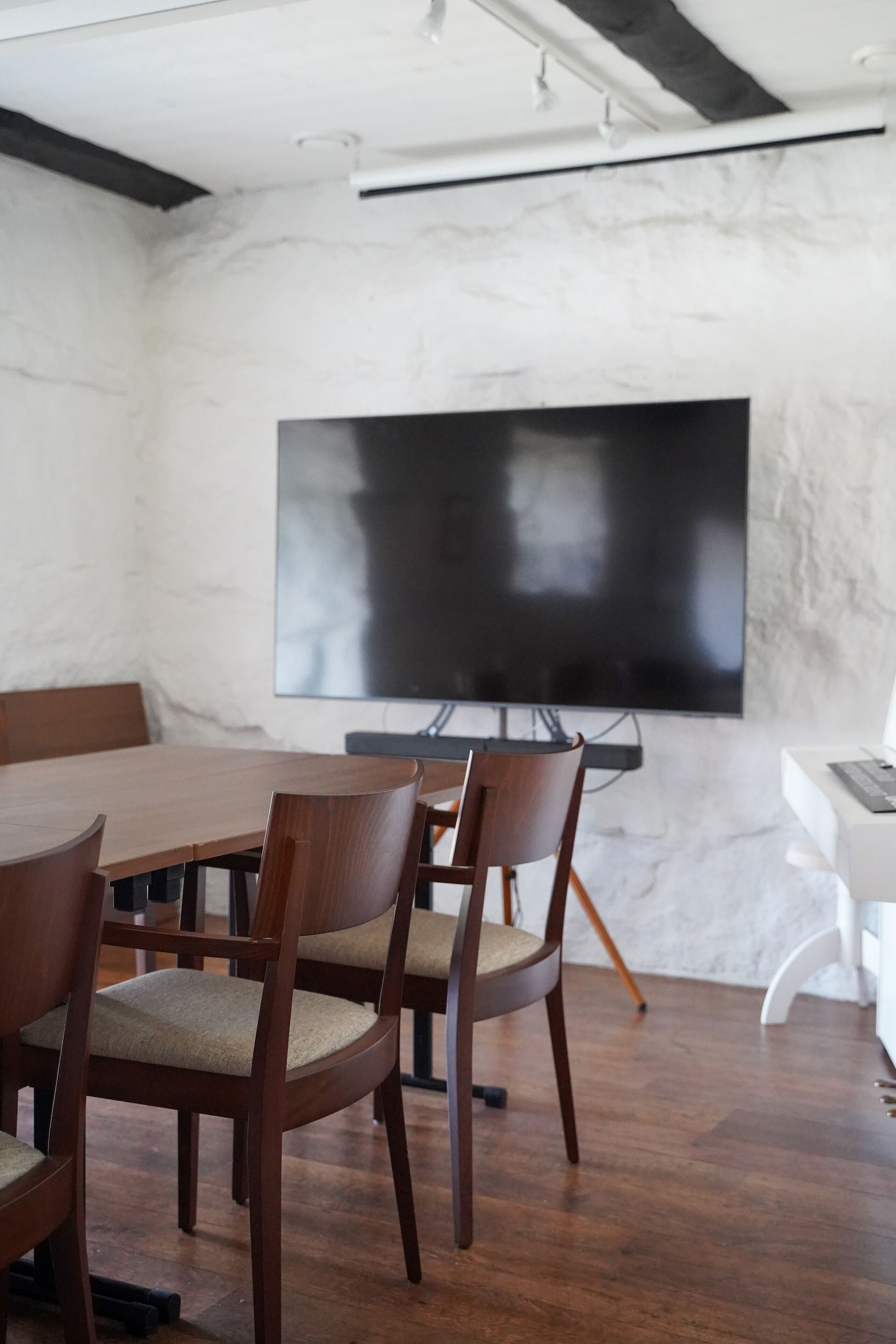 Un salón de conferencias con un televisor de pantalla plana grande, sillas de madera, una mesa de madera y un sofá blanco.
