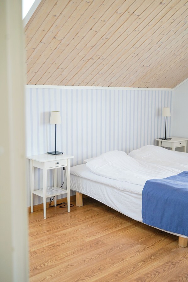 A bedroom with a sloped ceiling, a bed with white bedding, two bedside tables with lamps, and a striped wall.