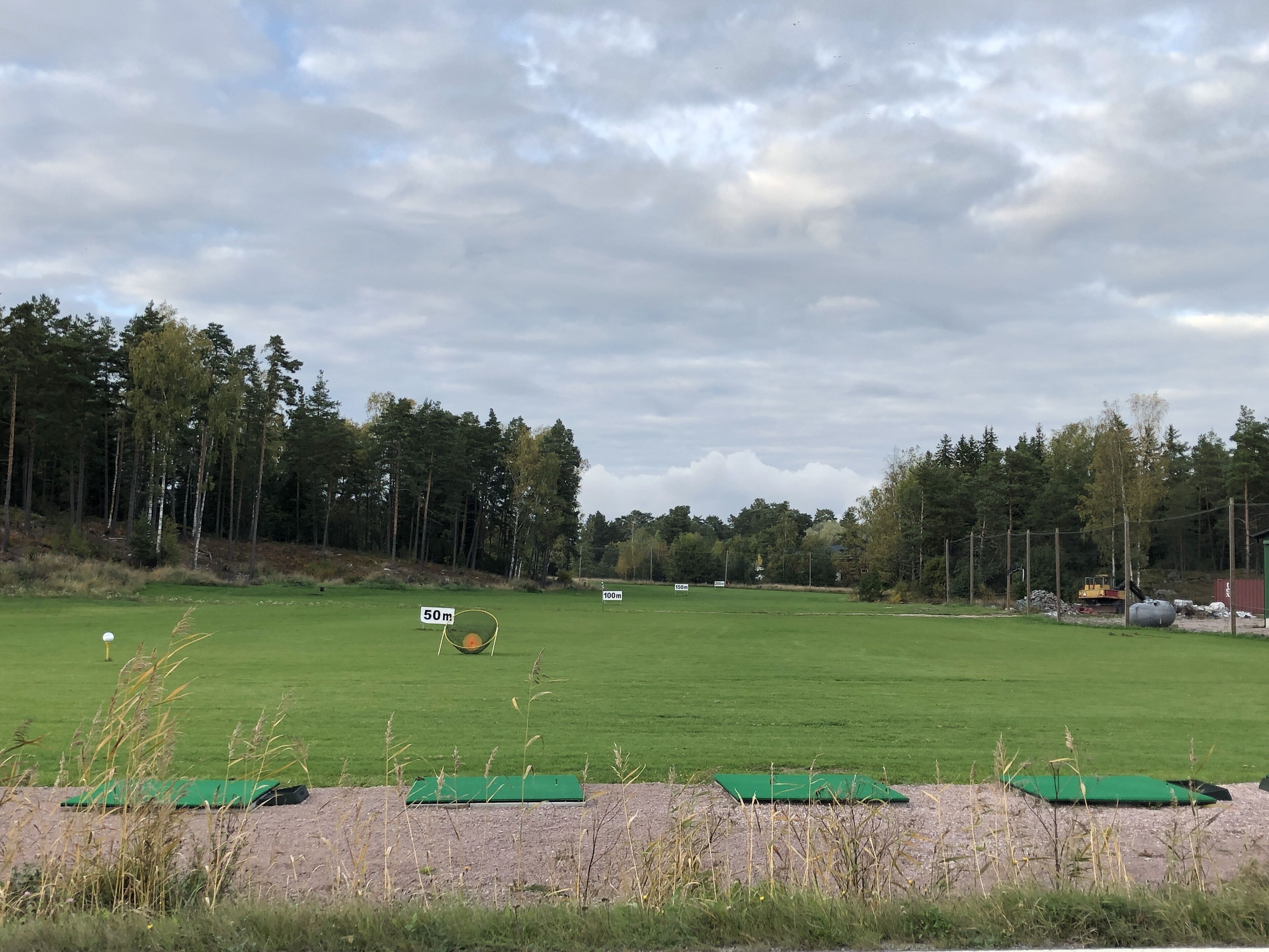 Um campo de golfe com gramado verde, árvores e um edifício ao longe.