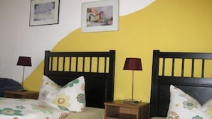 Habitación con dos camas, cada una con ropa de cama floral y cabeceros de madera. Hay dos mesitas de noche con lámparas.