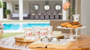 Une table en bois sur laquelle se trouvent un livre, des lunettes, des tasses à thé et un présentoir à gâteaux avec des pâtisseries.