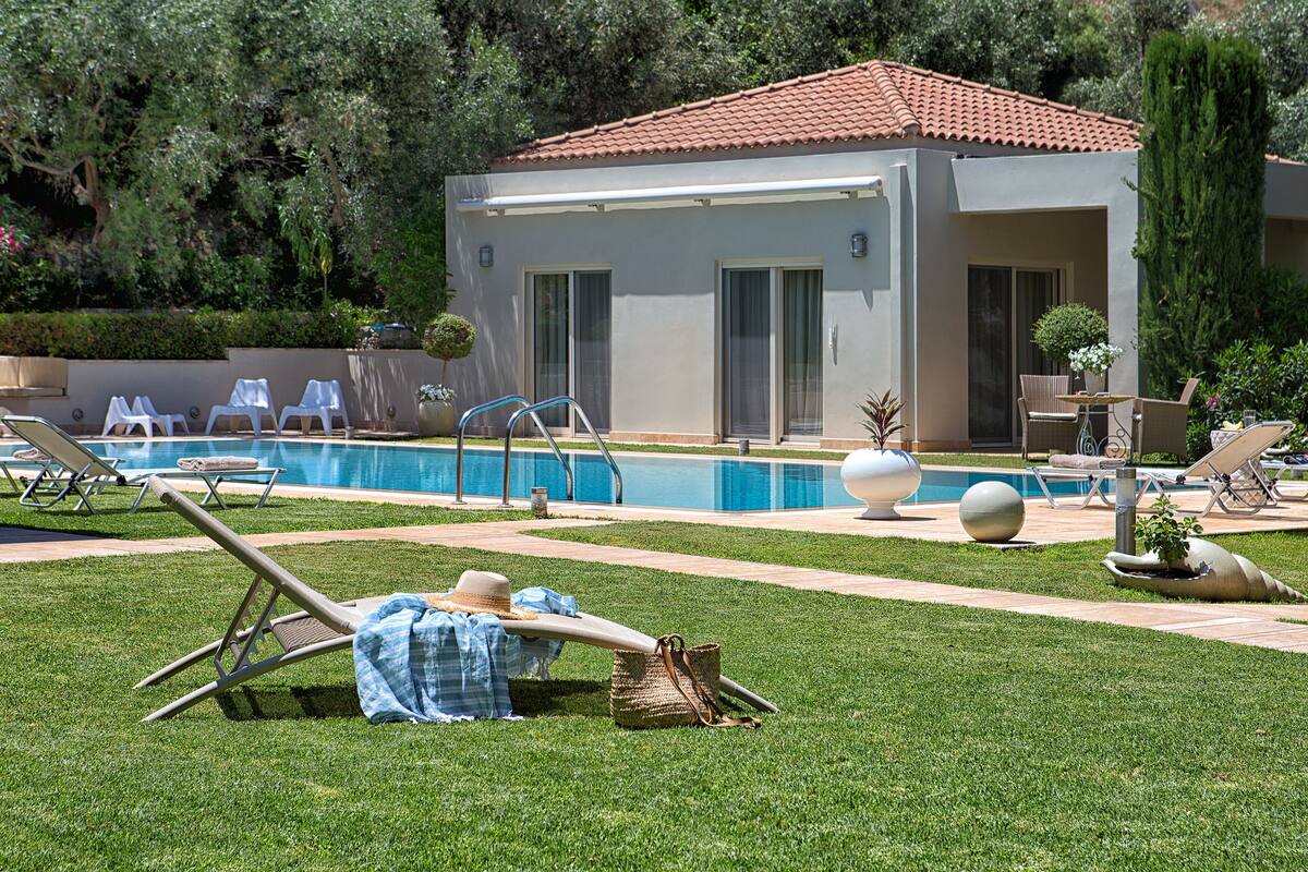 A poolside area with lounge chairs, a small building with a tiled roof, and a swimming pool.