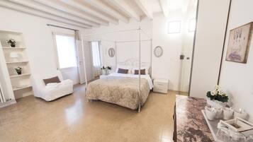 Une chambre à coucher avec un lit à baldaquin, une chaise blanche, une table en marbre et une fenêtre avec des rideaux.