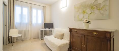 A living room with a white sofa, a wooden cabinet, a television, and a painting of flowers on the wall.