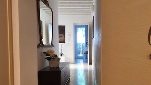 A hallway with a wooden door, a dark wooden bench with a basket of flowers, a mirror on the wall, and a door leading to another room.