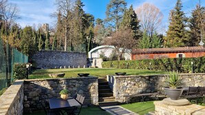 A stone patio with a table and chairs, surrounded by a well-maintained lawn and stone walls.