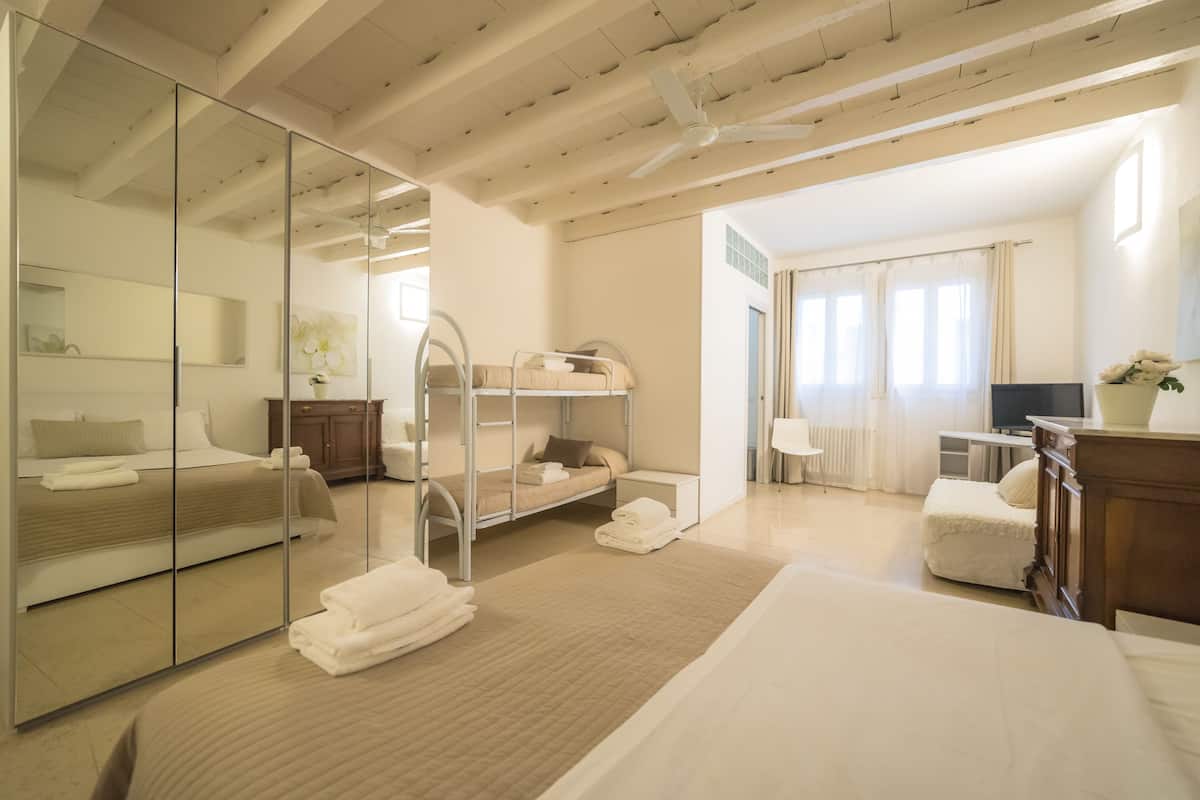 Ein Hotelzimmer mit einem großen Bett, einem kleineren Bett, einem Schreibtisch, einem Stuhl, einem Spiegel und einem Kleiderschrank.