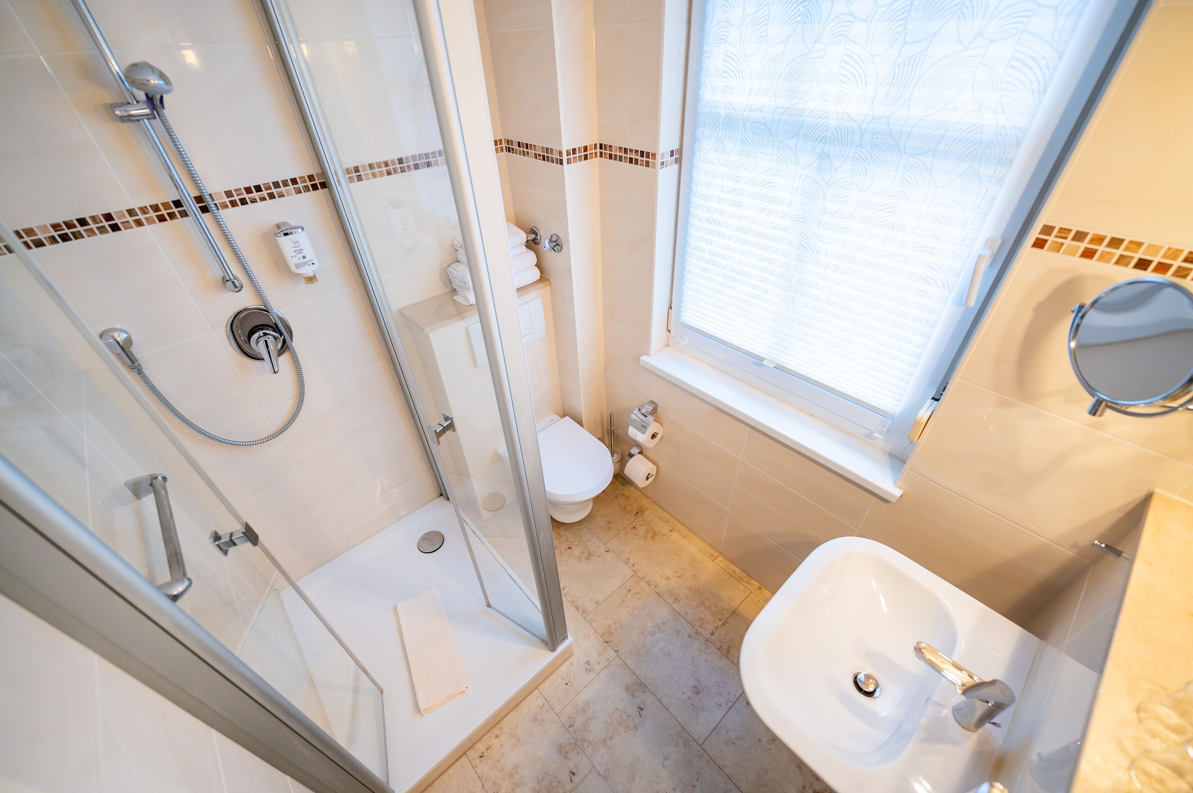 A bathroom with a glass-enclosed shower, a toilet, a sink, and a window.