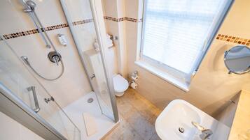 A bathroom with a glass-enclosed shower, a toilet, a sink, and a window.
