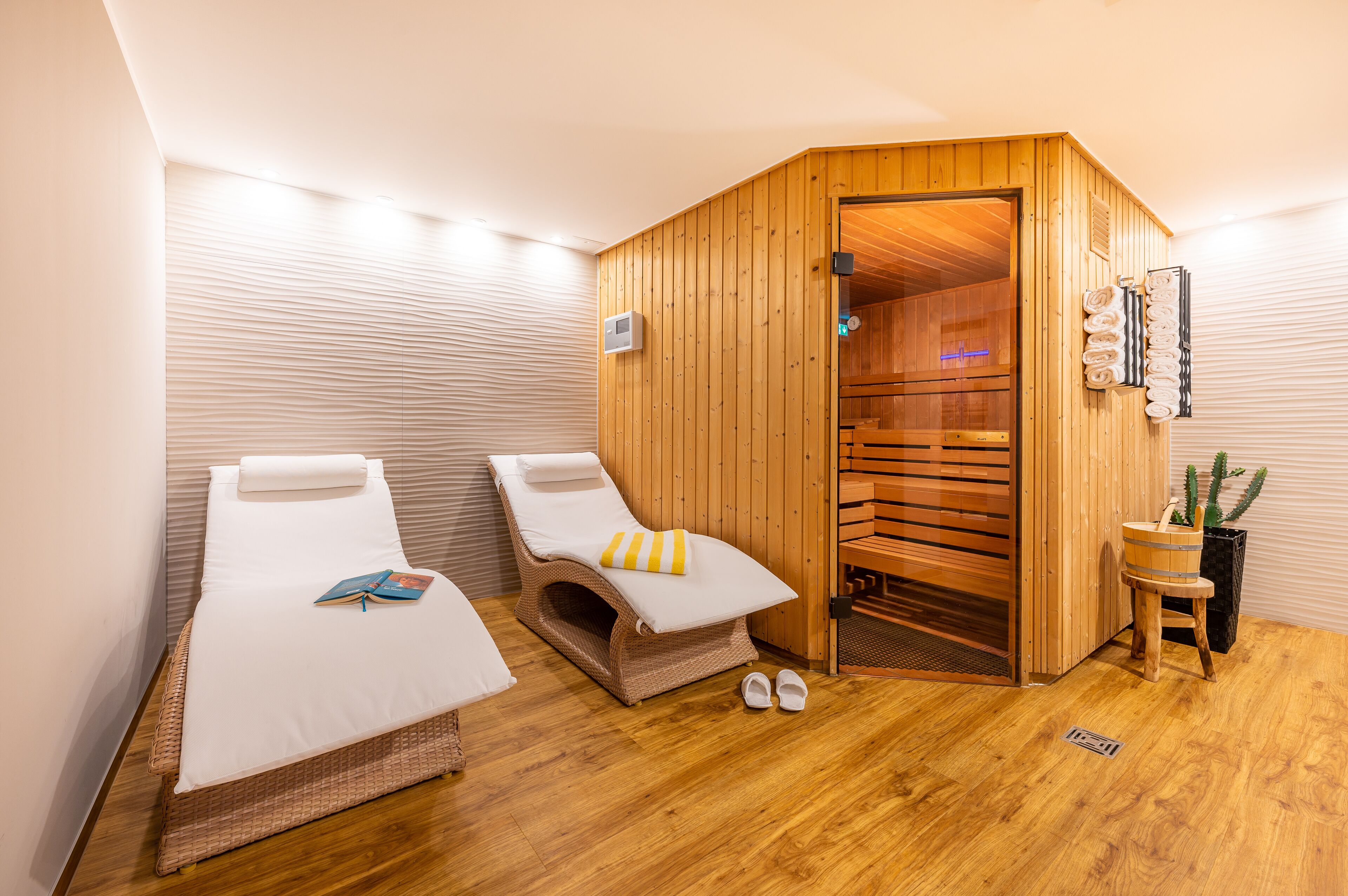 Una stanza con due letti, una sauna in legno e un piccolo tavolo con un cactus.