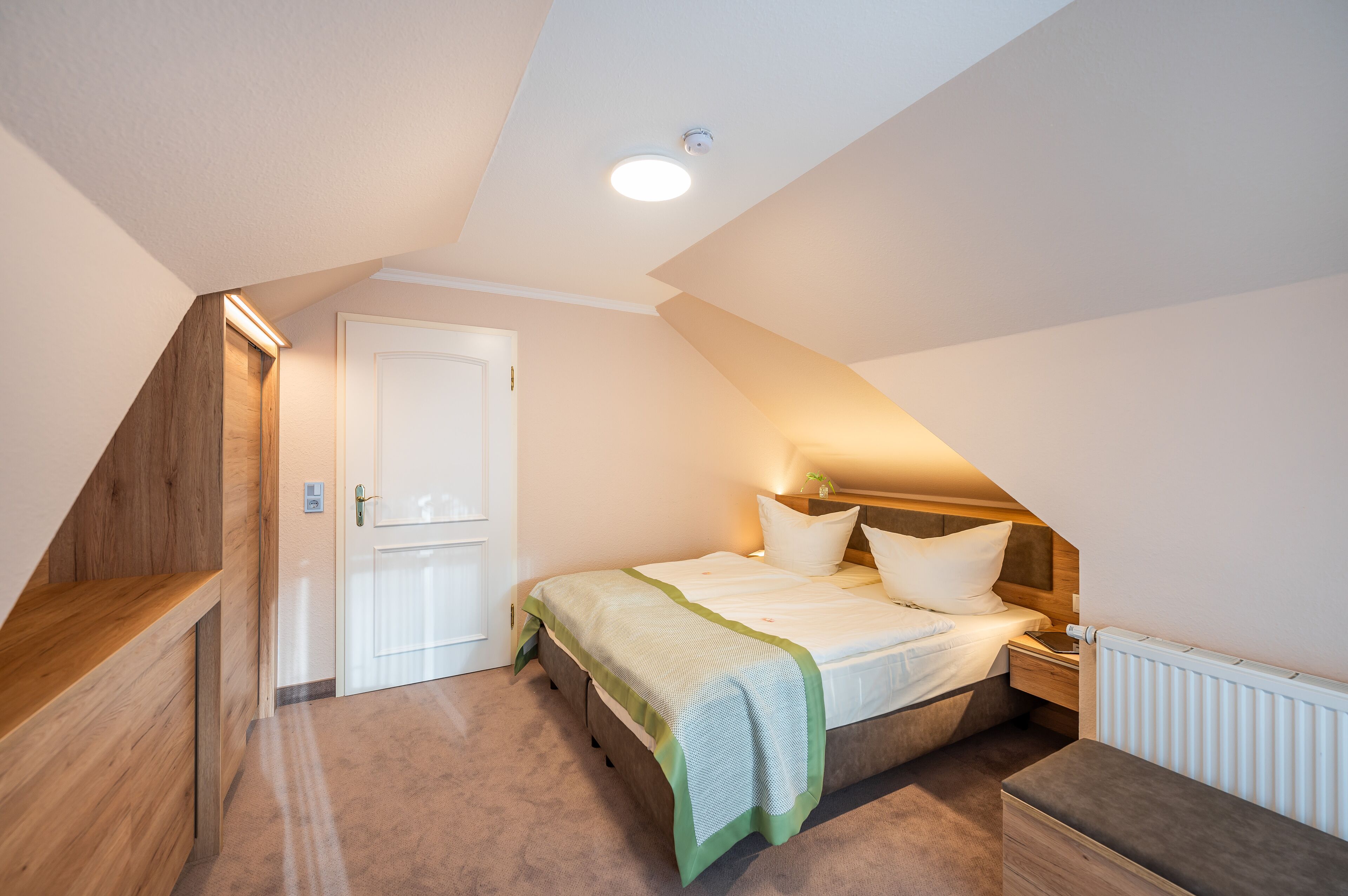 A bedroom with a sloped ceiling, a bed with a green and white bedspread, a bedside table, and a nightstand.