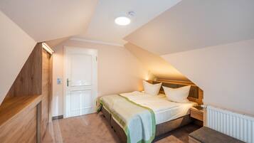 A bedroom with a sloped ceiling, a bed with a green and white bedspread, a bedside table, and a nightstand.