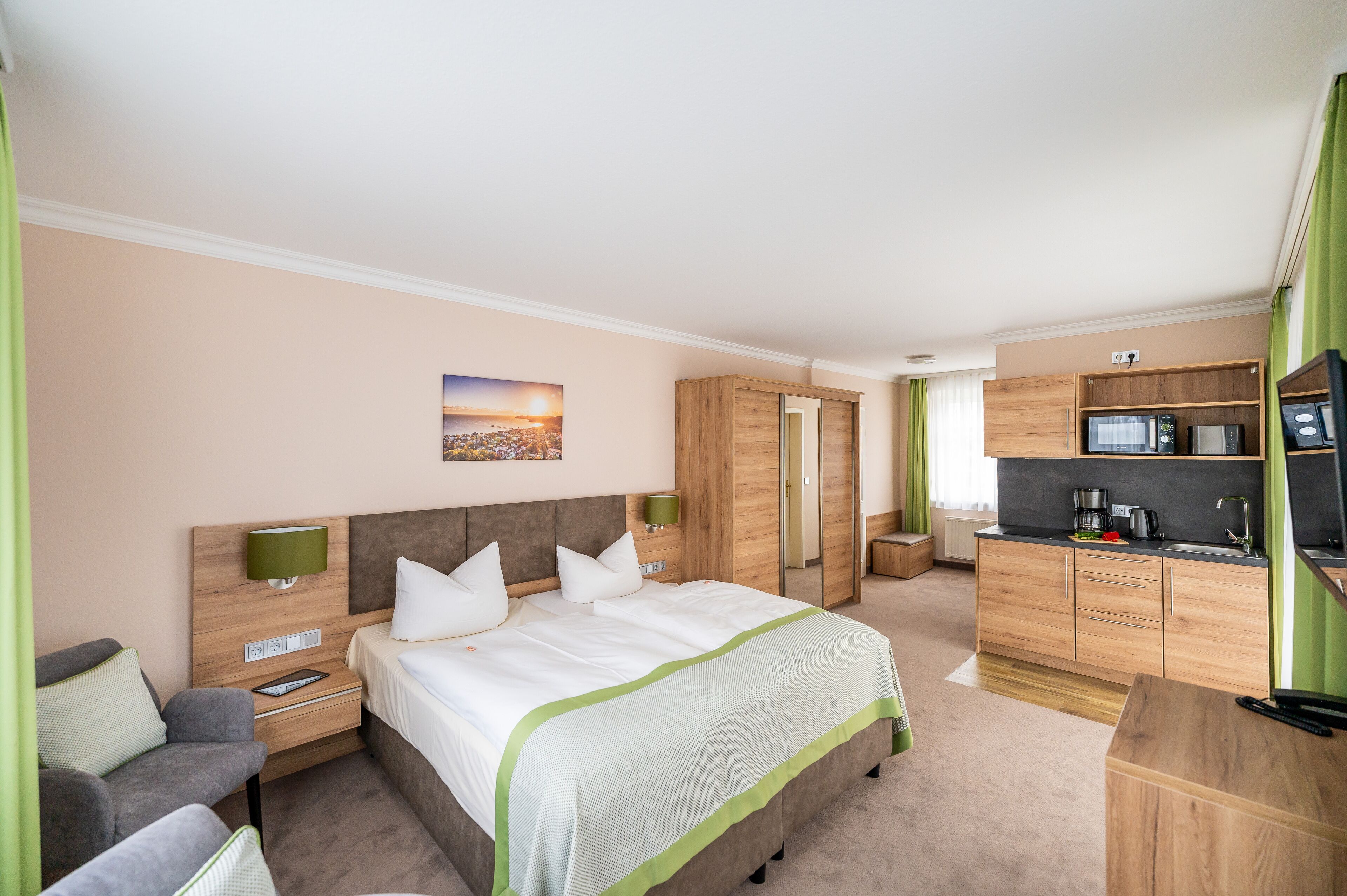 A hotel room with a bed, a desk, a chair, a wardrobe, and a kitchenette.