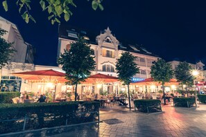 An outdoor cafe area with tables and chairs, surrounded by well-maintained hedges and trees. - Centralhotel Binz (Binz)