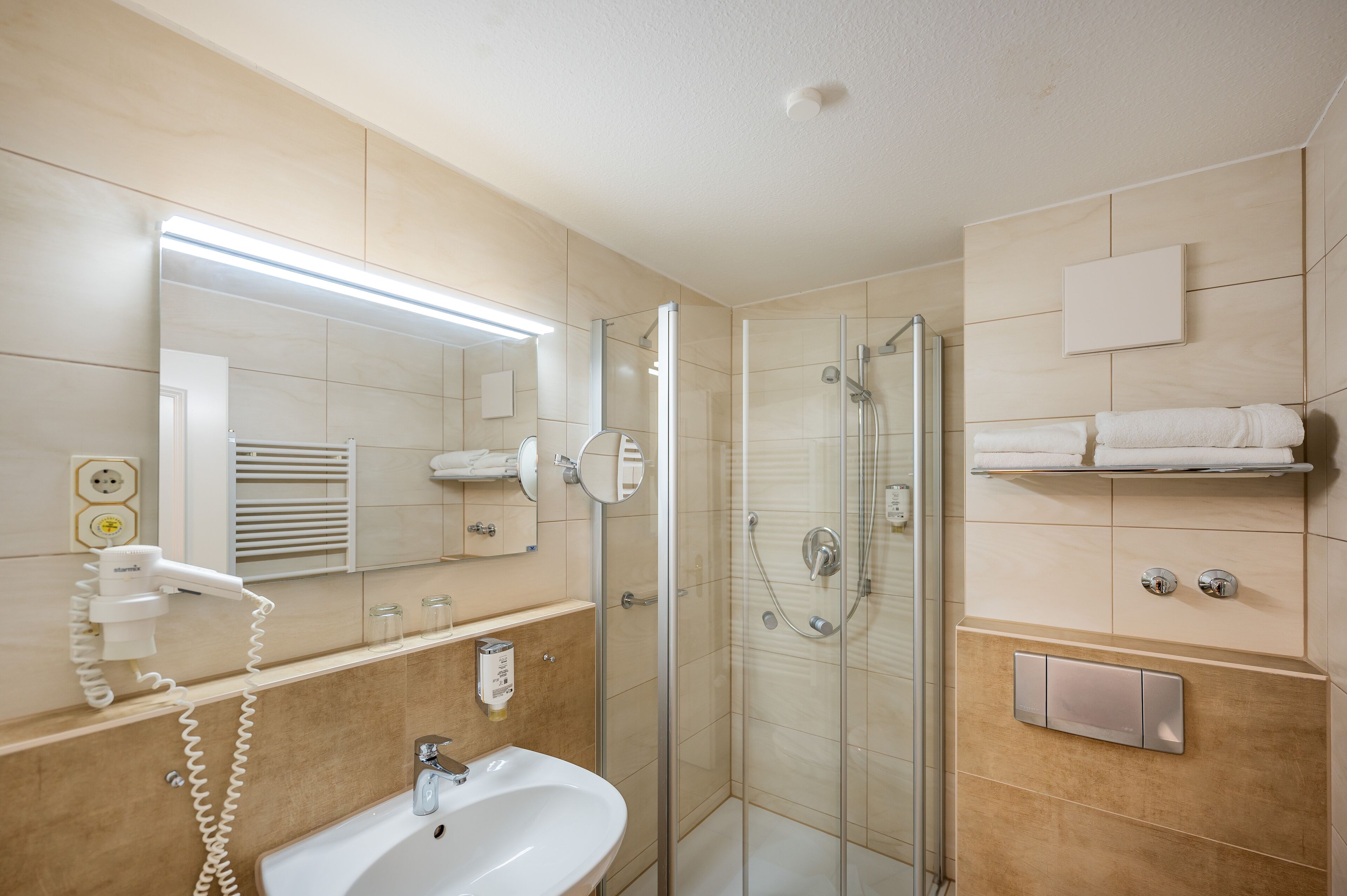 A modern bathroom with a glass shower enclosure, a white sink, a hairdryer, and a towel rack.