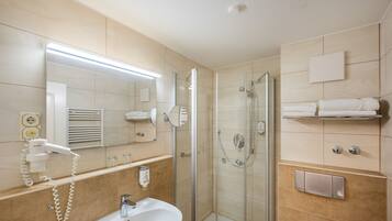 A modern bathroom with a glass shower enclosure, a white sink, a hairdryer, and a towel rack.