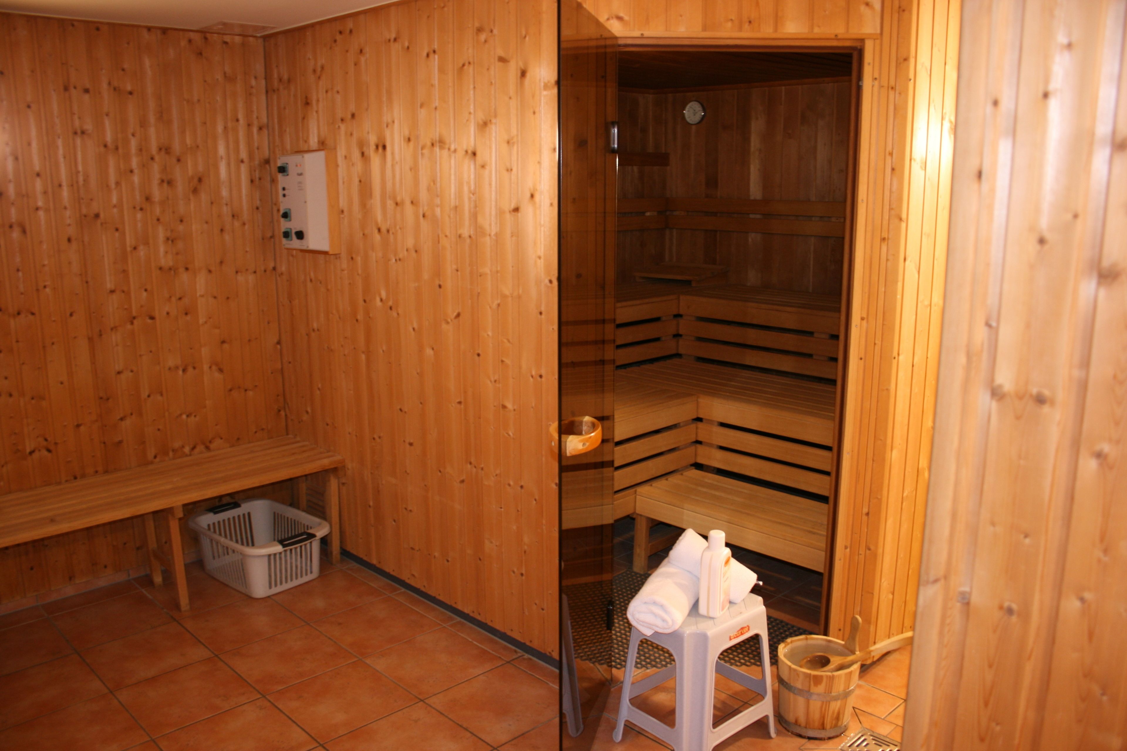 A sauna room with wooden walls and benches. There is a bench with a basket underneath and a stool with towels on it.