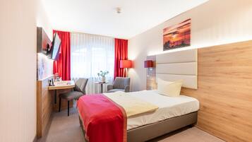Ett hotellrum med en säng, ett skrivbord, en stol, en tv och ett fönster med röda gardiner.