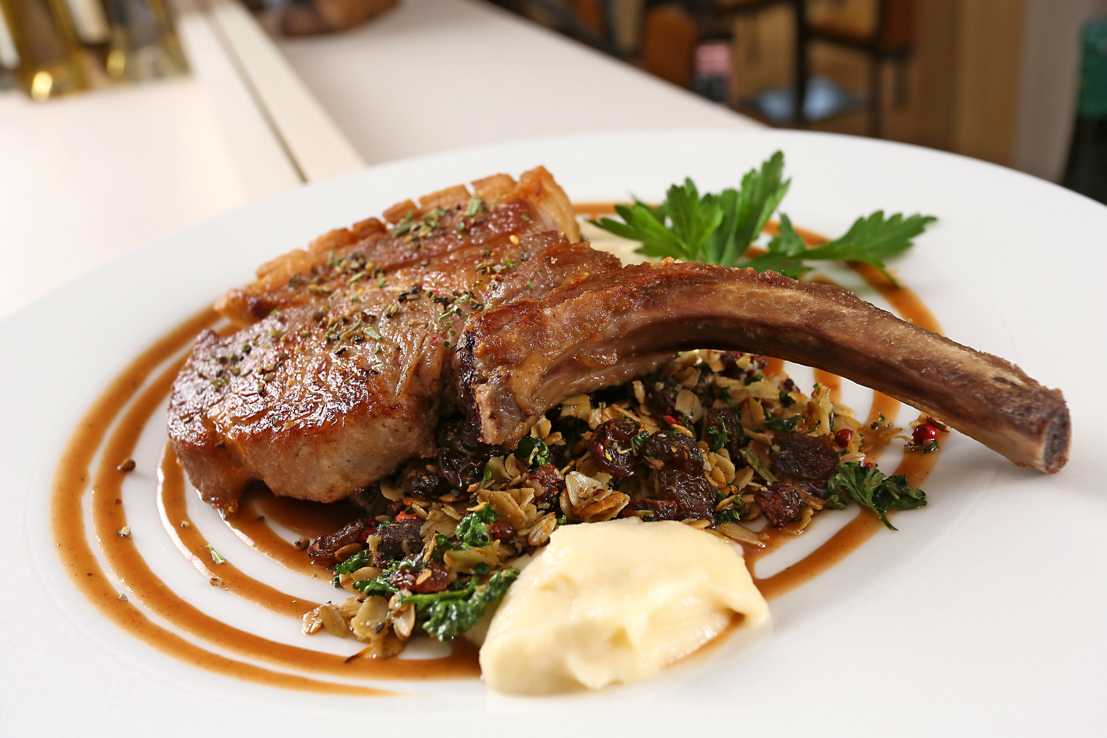 A plate of food with a lamb chop, greens, and a sauce.