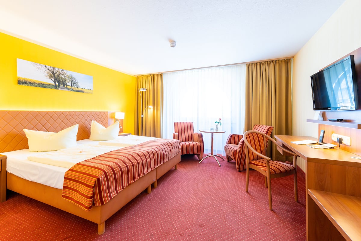 Une chambre d’hôtel avec un grand lit, un bureau avec une télévision, une chaise et une petite table.