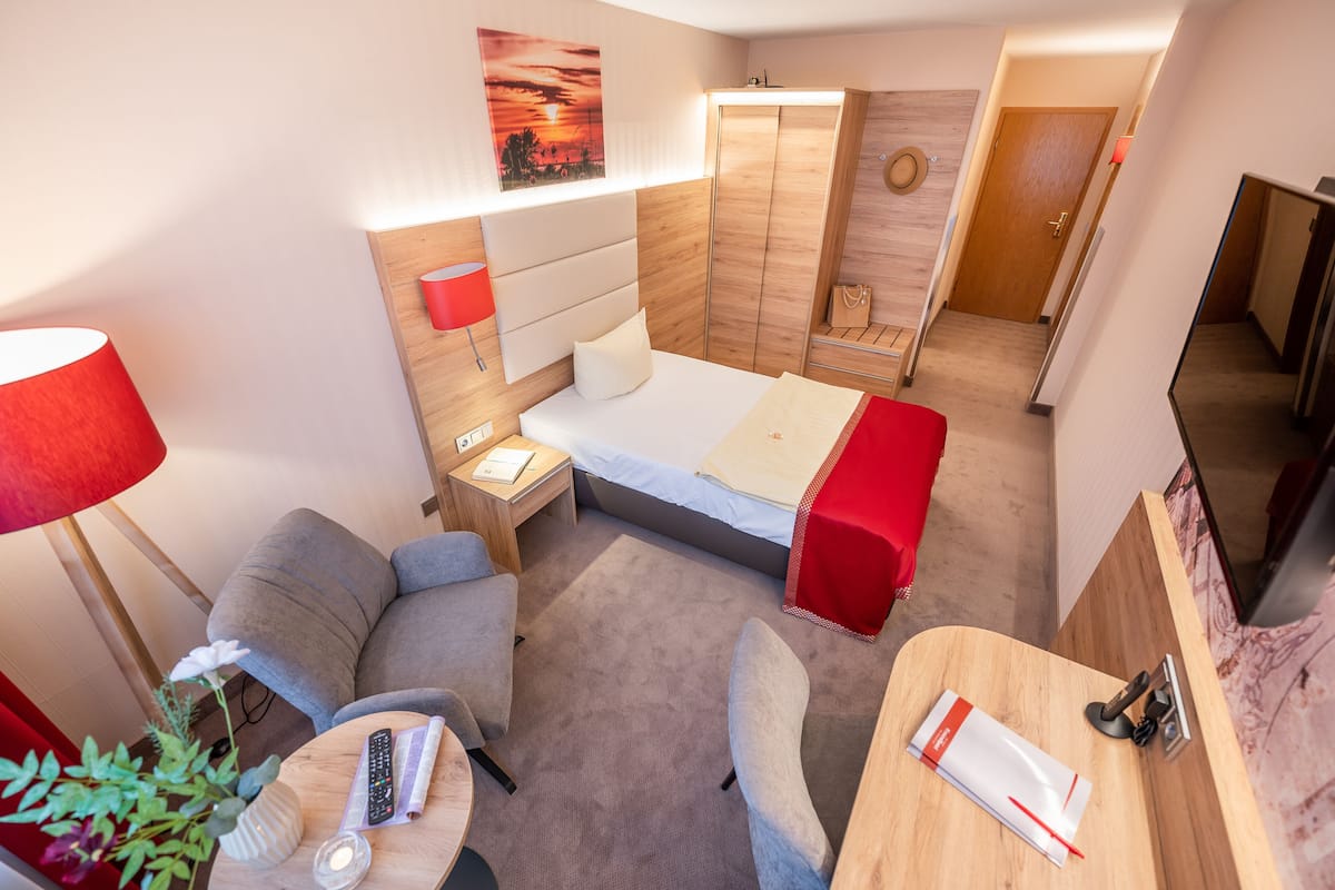Une chambre d’hôtel avec un lit, un bureau, une chaise, une lampe et une plante.