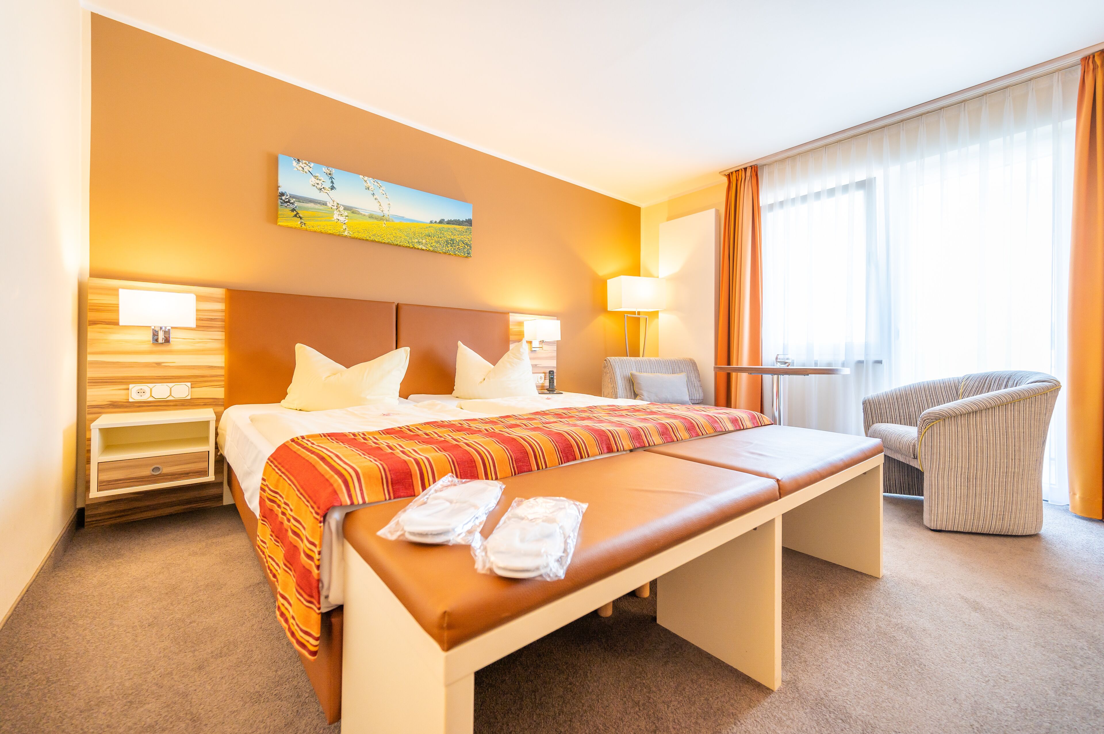 Ein Hotelzimmer mit einem großen Bett, einer Bank, einem Sessel und einem Gemälde an der Wand.