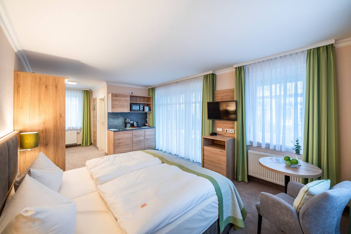 Une chambre d’hôtel avec un grand lit, un bureau, une chaise, une télévision et une kitchenette.
