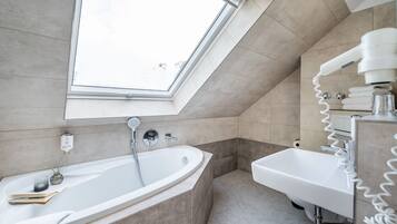 Une salle de bain moderne dotée d’un puits de lumière, d’une baignoire sur pieds, d’un lavabo et d’un porte-serviettes.