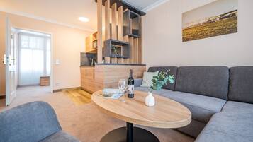 Una sala moderna con un sofá gris, una mesa de centro de madera y una cocina al fondo.