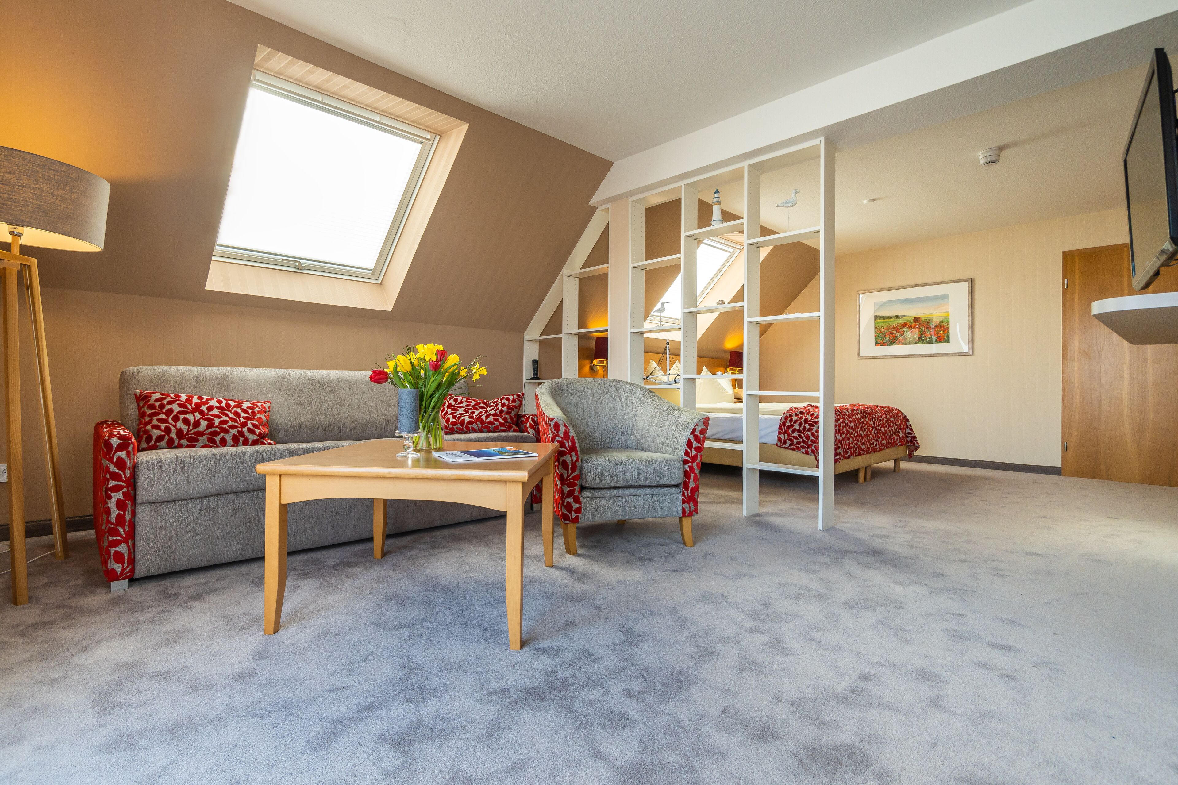 A loft-style room with a high ceiling, a skylight, a sofa, a chair, a table, and a bed.