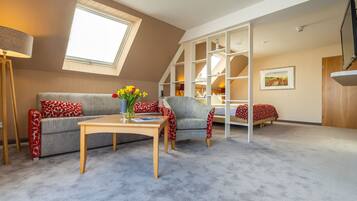 A loft-style room with a high ceiling, a skylight, a sofa, a chair, a table, and a bed.