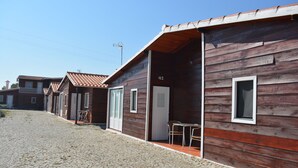 A row of wooden cabins with tiled roofs, a cobblestone path, and a clear blue sky. - Lusitaurus (Redondo)