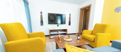Una sala de estar moderna con sillones amarillos, un sofá gris, una mesa de centro de madera y un televisor de pantalla plana montado en la pared.