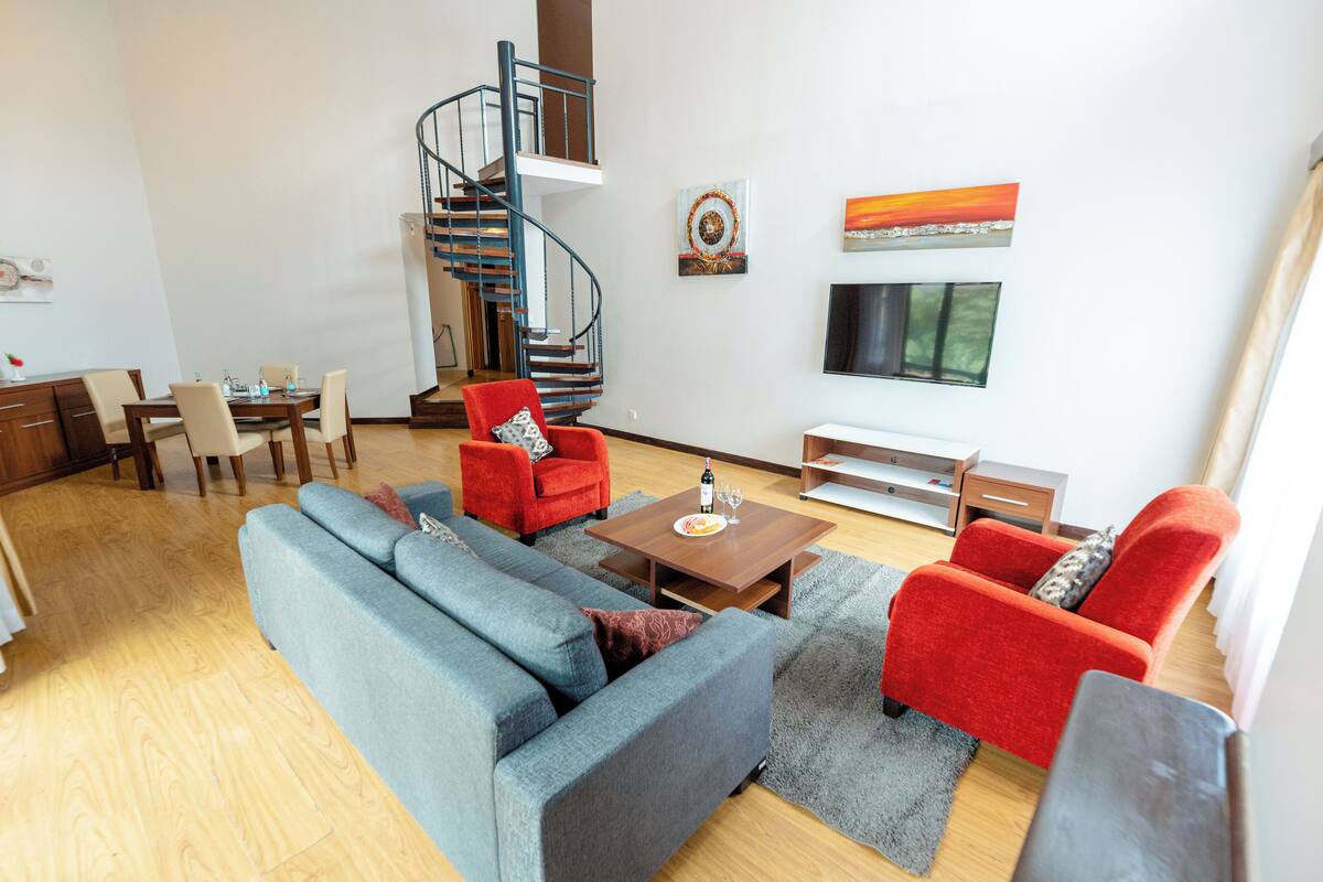 A modern living room with a blue sofa, red armchairs, a wooden coffee table, and a spiral staircase.