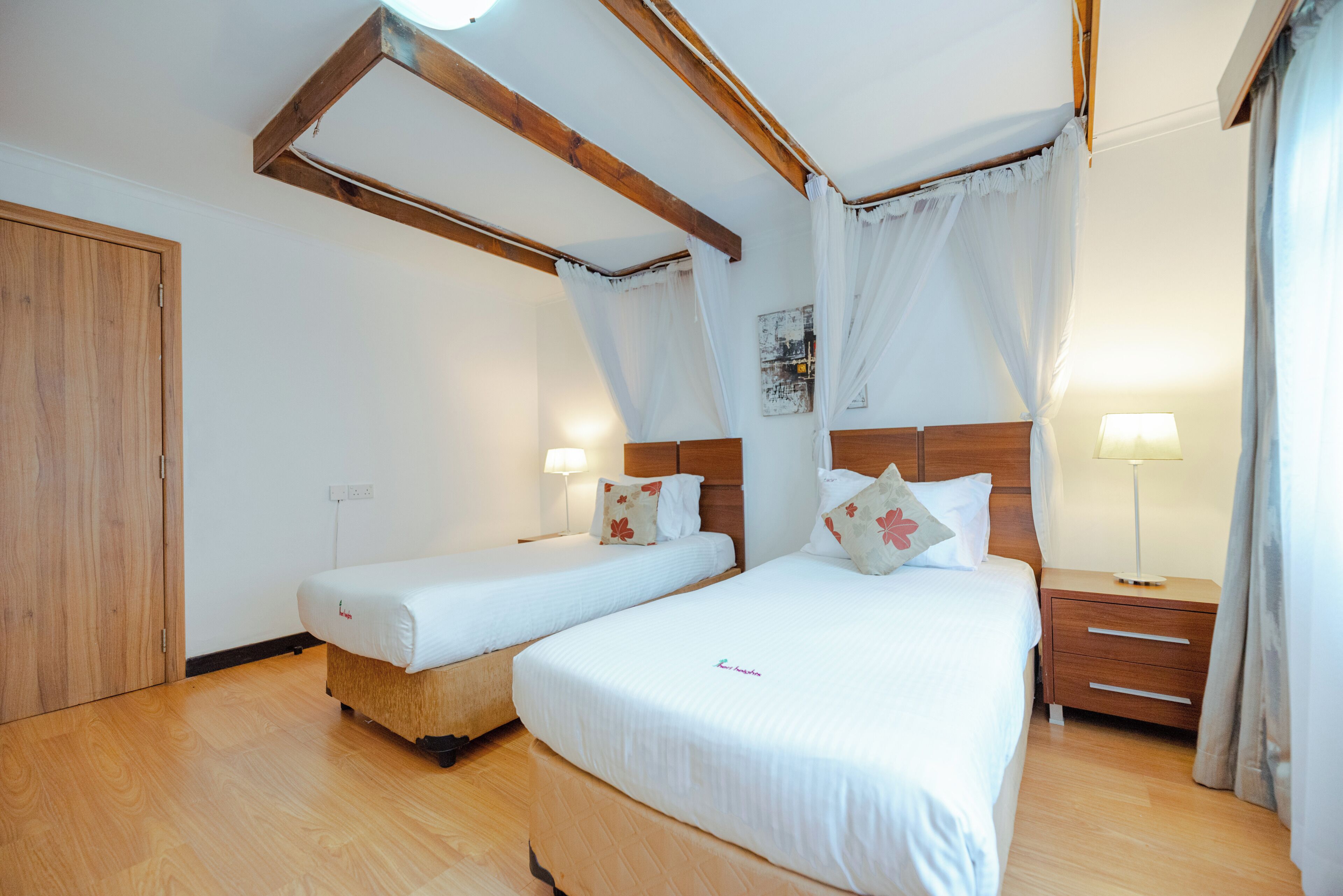A double room with two beds, wooden beams, a nightstand, and a bedside table.