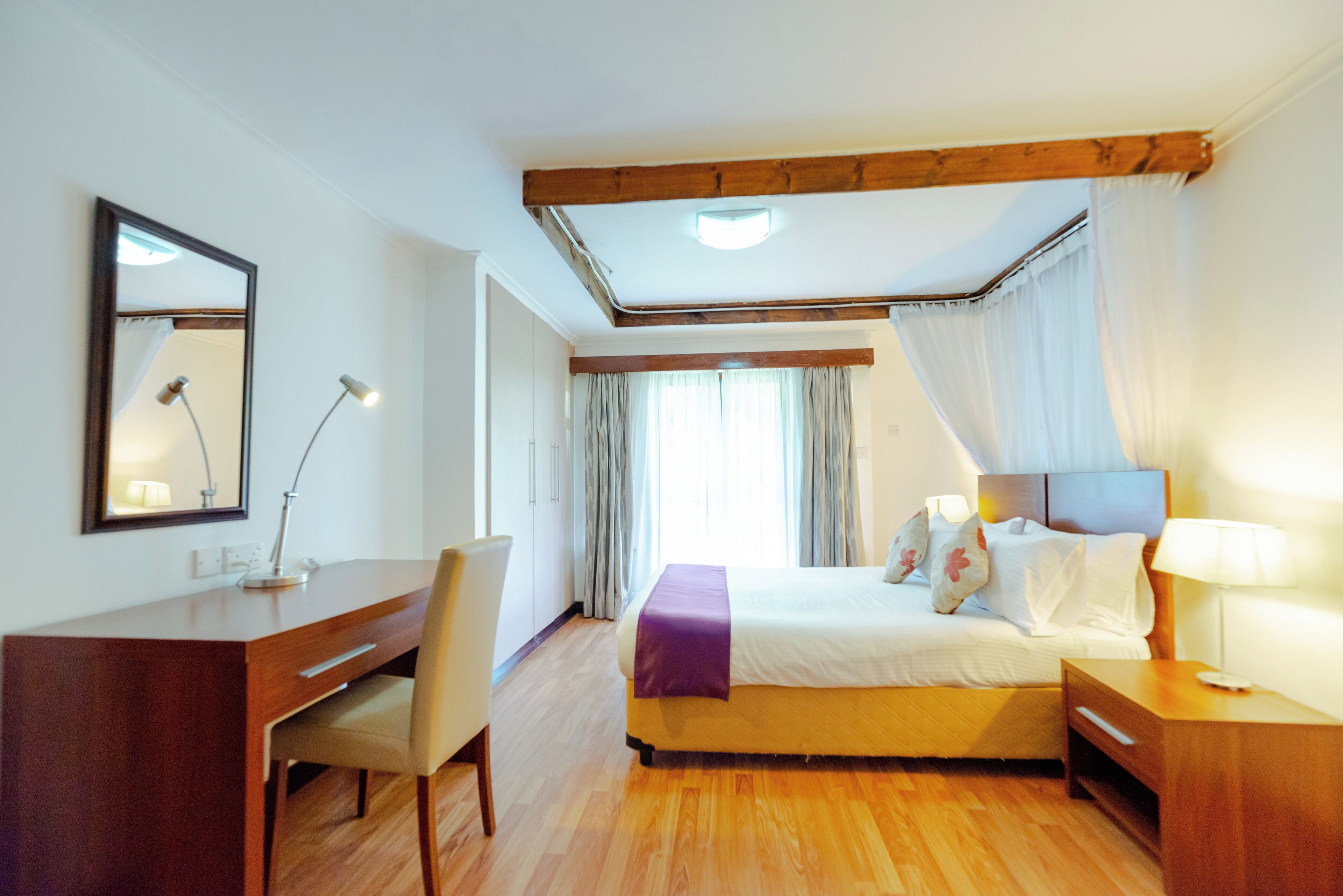 Ein Hotelzimmer mit Bett, Schreibtisch, Stuhl, Nachttisch, Lampe und Spiegel.