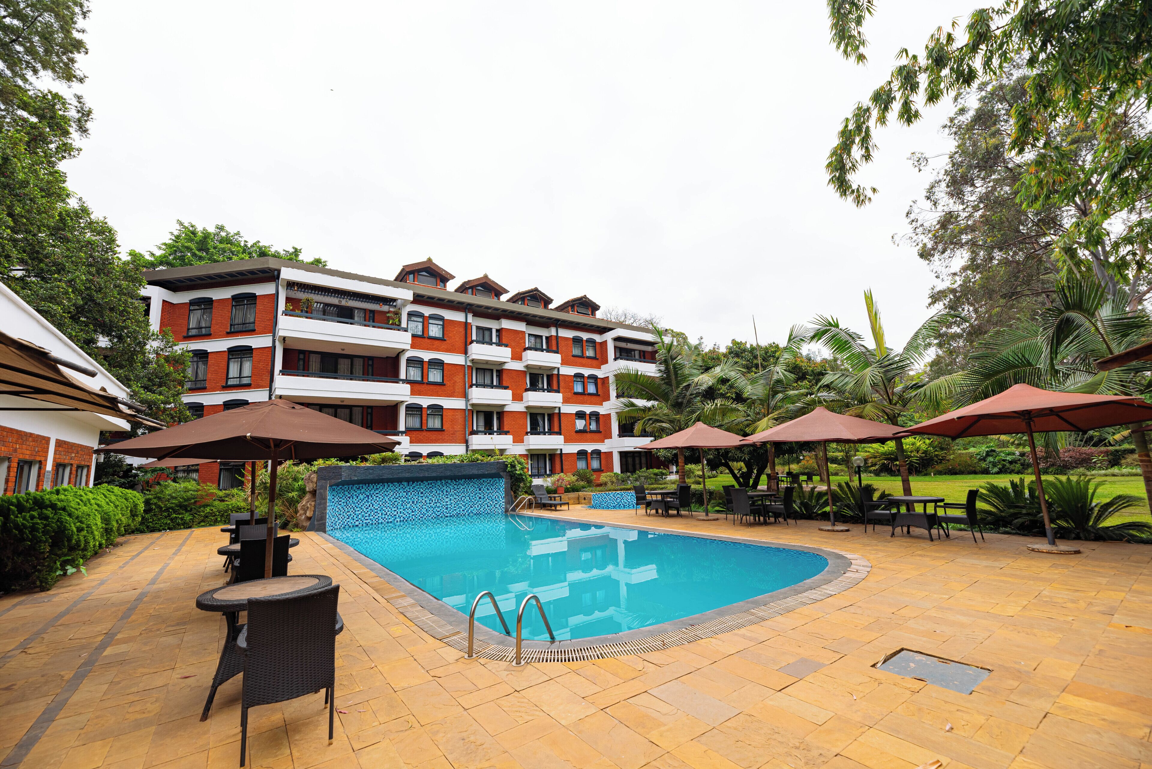 Un hotel con piscina, mobiliario exterior y abundante vegetación.