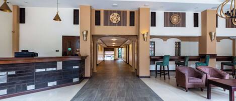 A hotel lobby with a reception desk, seating area, and a long corridor leading to other rooms.