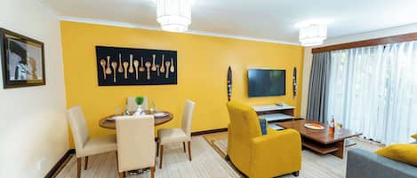 Una sala de estar moderna con una pared de acento amarilla, un comedor con una mesa redonda y sillas, un sofá, un televisor y un gran ventanal con cortinas.