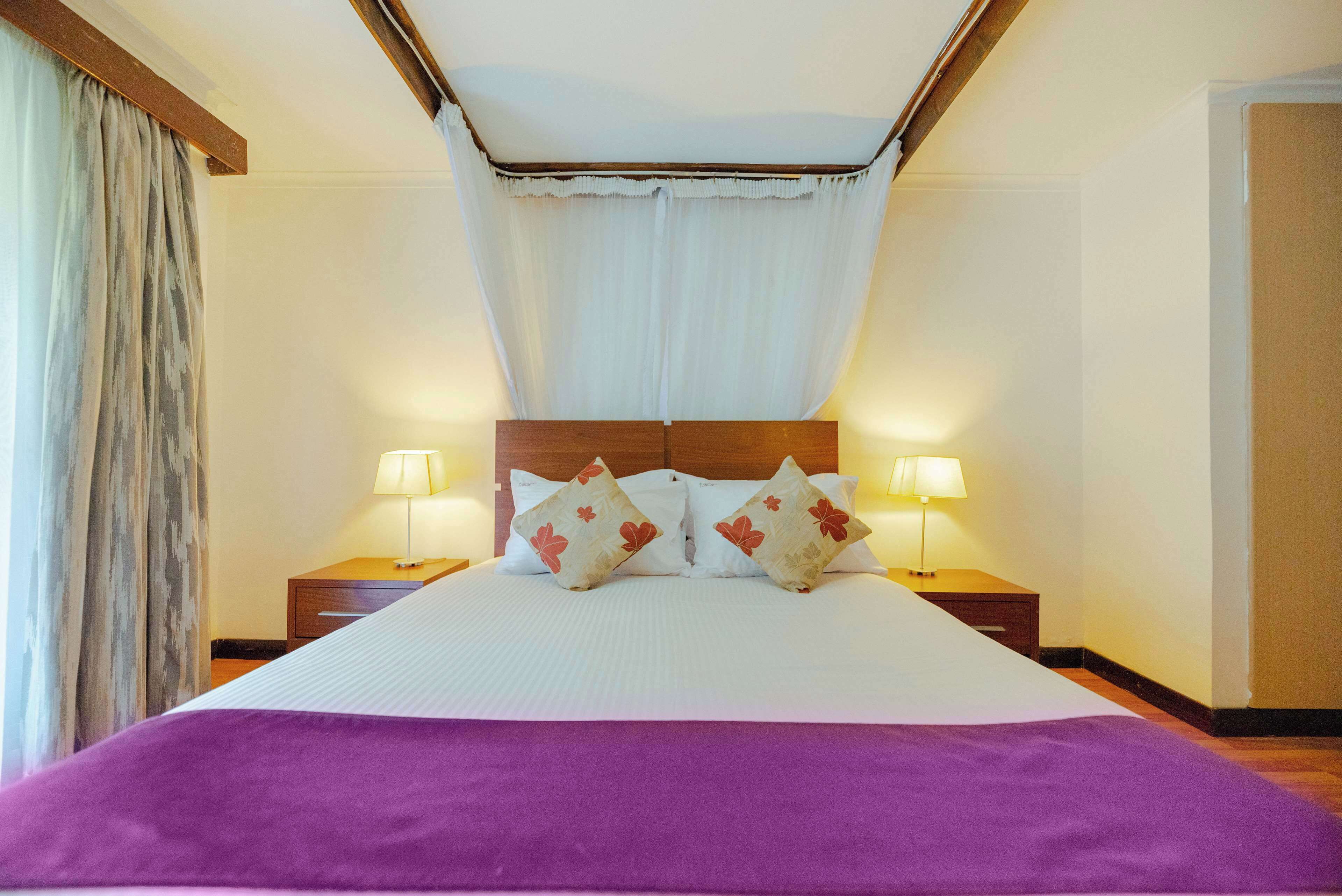 A neatly made bed with a purple bedspread, two bedside lamps, and decorative pillows.
