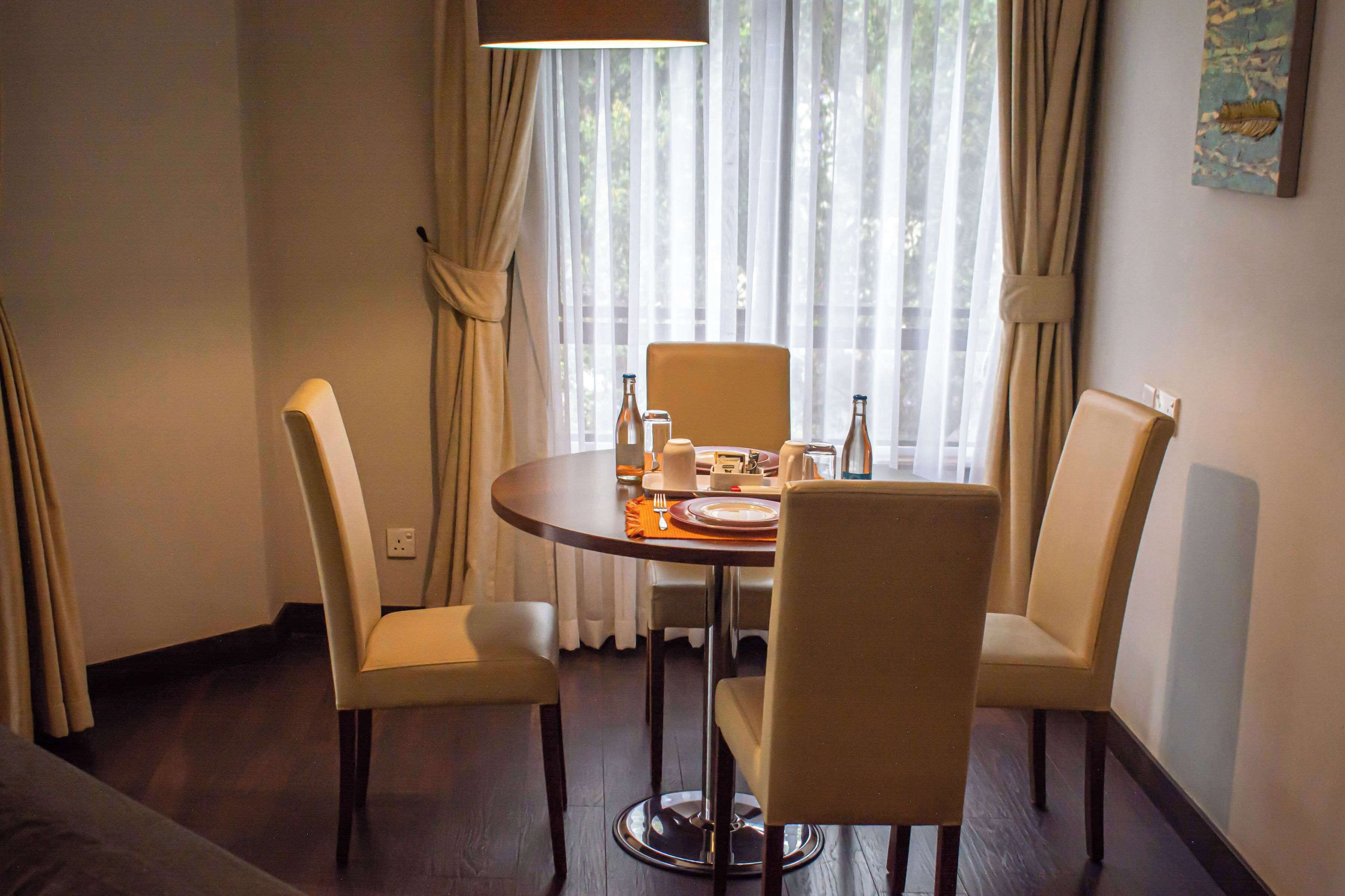 A dining area with a round table, four chairs, and a window with curtains.