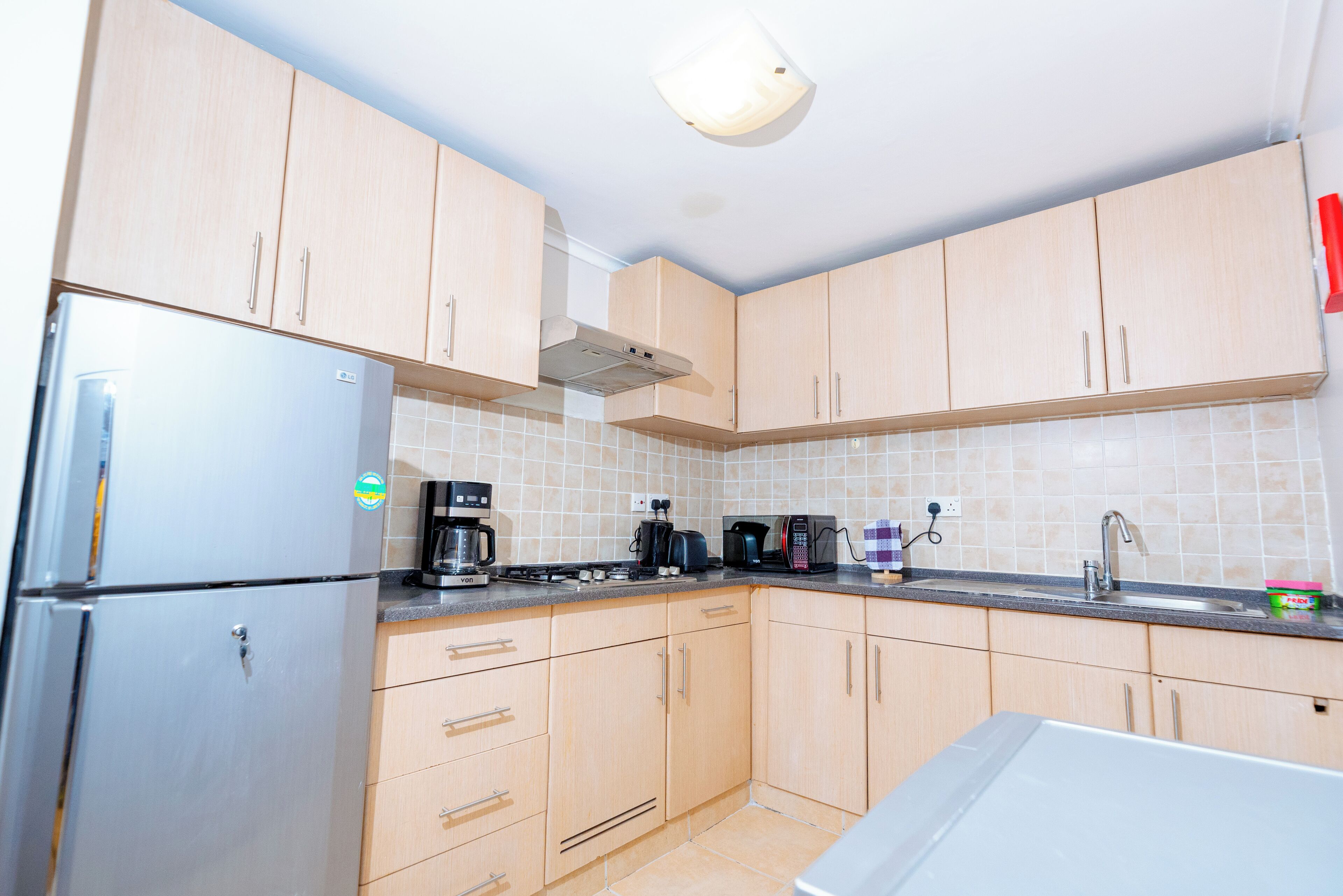 A kitchen with light wooden cabinets, a stainless steel refrigerator, a coffee maker, and a microwave.
