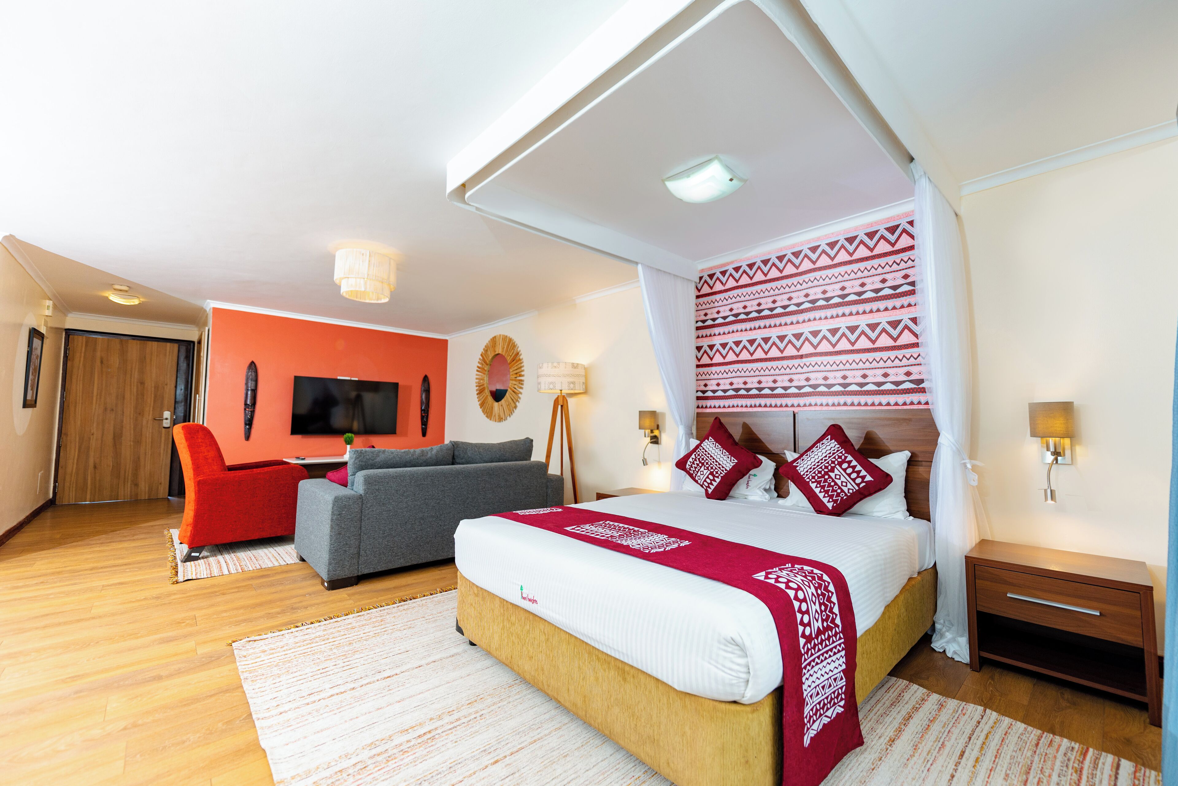 A modern hotel room with a large bed, a sofa, a TV, and a wooden floor.
